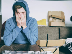 Junger Mann sitzt auf der Couch und reibt sich müde die Augen